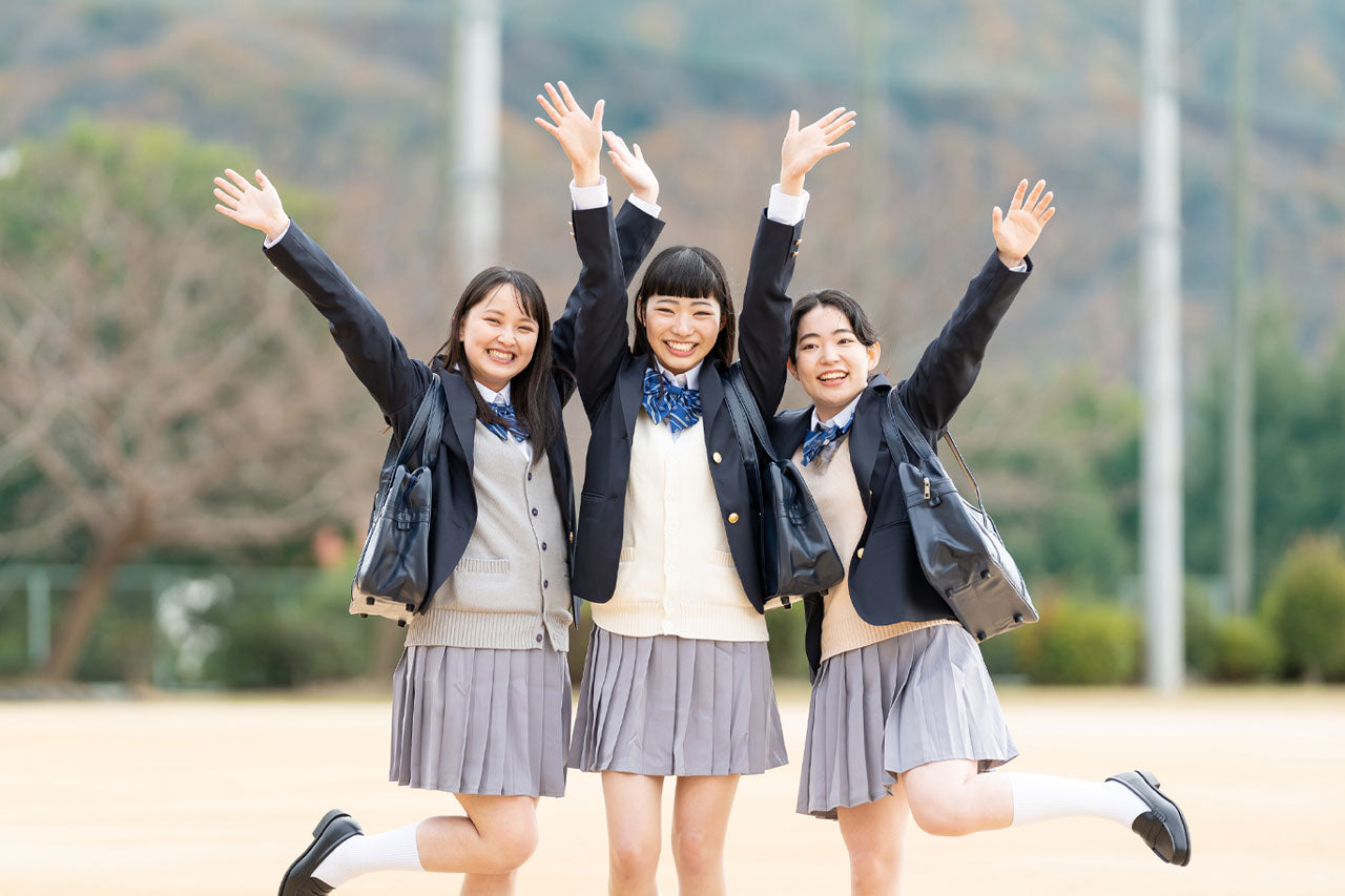 冬の制服を着た3人の日本人高校生が屋外でポーズをとっている、楽しそうな表情をしている。真ん中の女性は若いころの花嫁です。