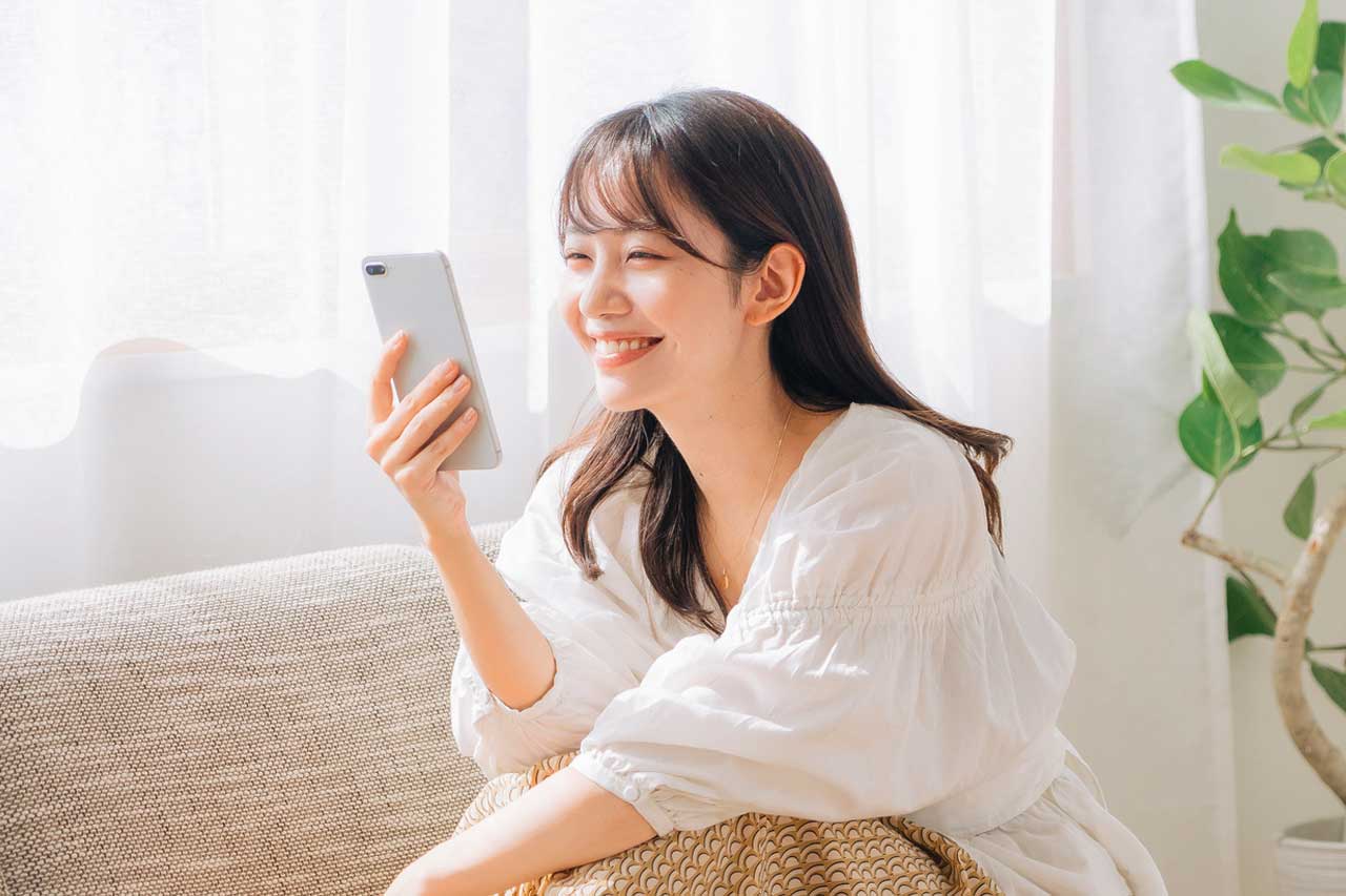 結婚を考えている若い女性がスマートフォンでプロフィールムービーを閲覧し、幸せそうにしています。