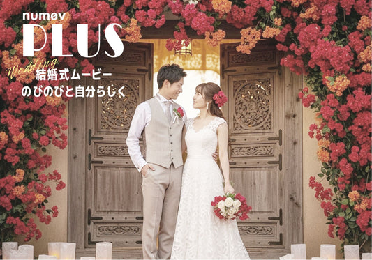 鮮やかな赤とオレンジのブーゲンビリアのアーチに囲まれた、華やかな木製の扉の前で抱き合う新郎新婦。足元にはキャンドルと花びらが飾られています。